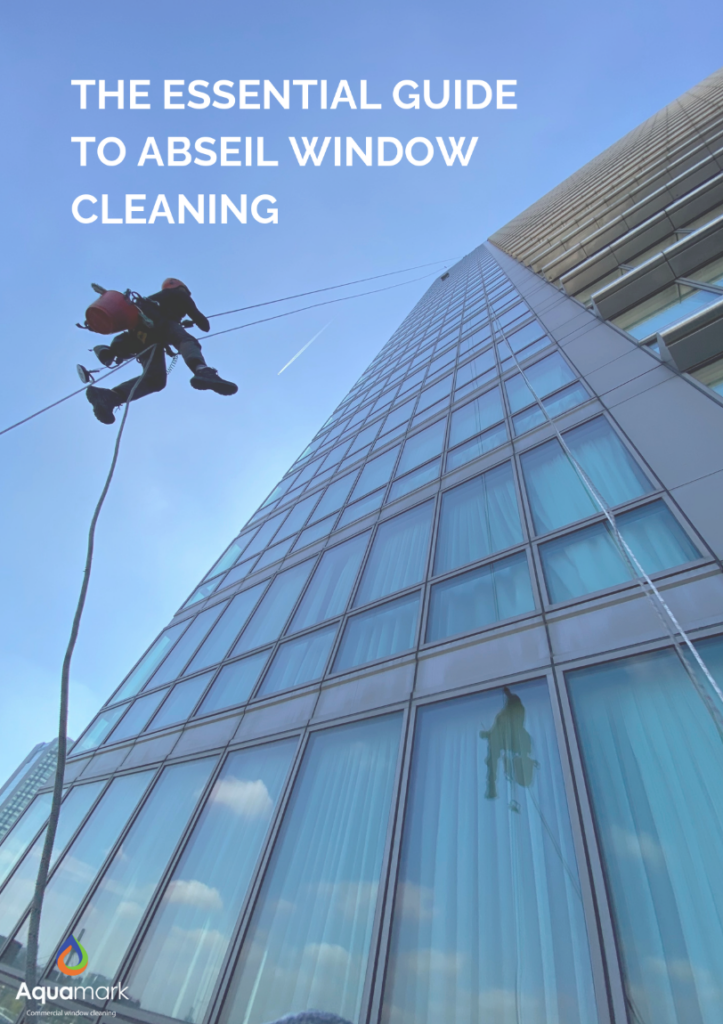 Climber suspended by ropes cleans a tall glass building as a guide cover, with bold white title text and a blue sky; Aquamark logo bottom-left.