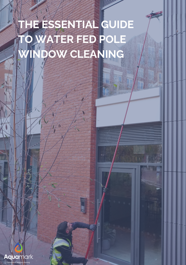 Window cleaner with a water-fed pole cleaning a glass storefront; overlay text: 'The Essential Guide to Water Fed Pole Window Cleaning' with Aquamark logo.